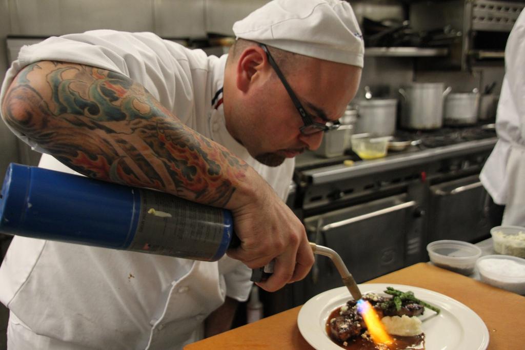 Culinary student Juan Hernandez torches a New York steak for lunch at the Norseman restaurant. (Chris Corbin/The Inquirer)