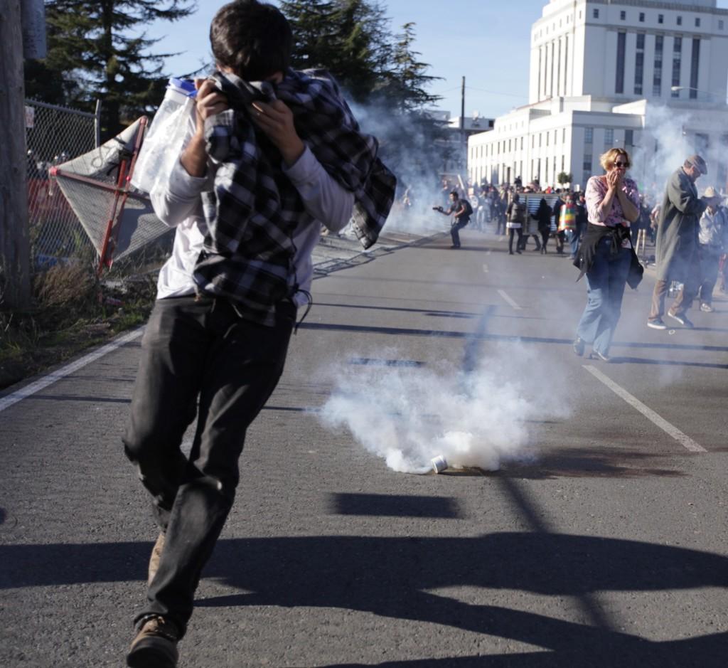 A protester runs from a smoke grenade thrown by police as they attempted to disperse an unruly crowd outside of Henry J. Kaiser Convention Center in Oakland on Saturday 1/28. (Mike Alfieri/ The Inquirer)