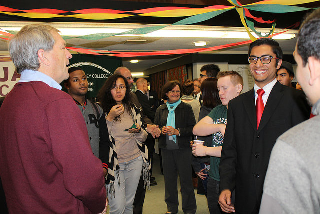 Congressman in red sweater talks with student in suit.