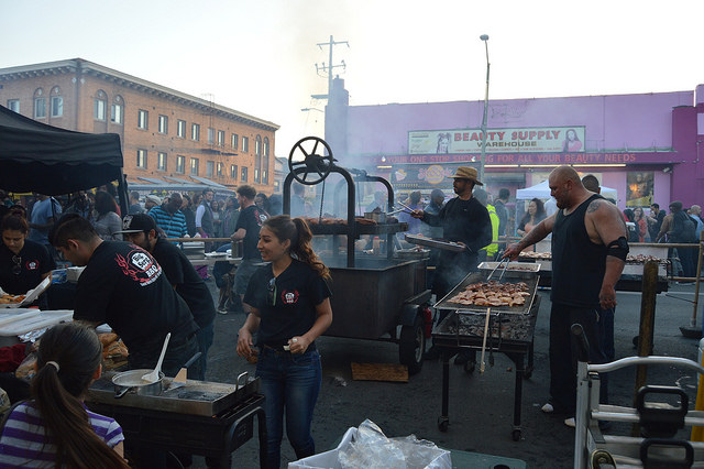 Man grilling, woman selling, crowd buying.