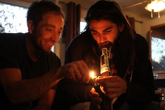 Two friends enjoy  cannabis using a water pipe, while assisting one another in their shared elation. 