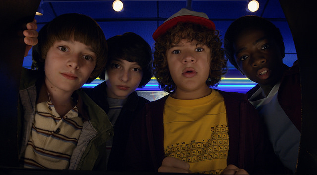 Noah Schnapp, FInn Wolfhard, Gaten Matarazzo, Caleb Mclaughlin staring at an arcade game